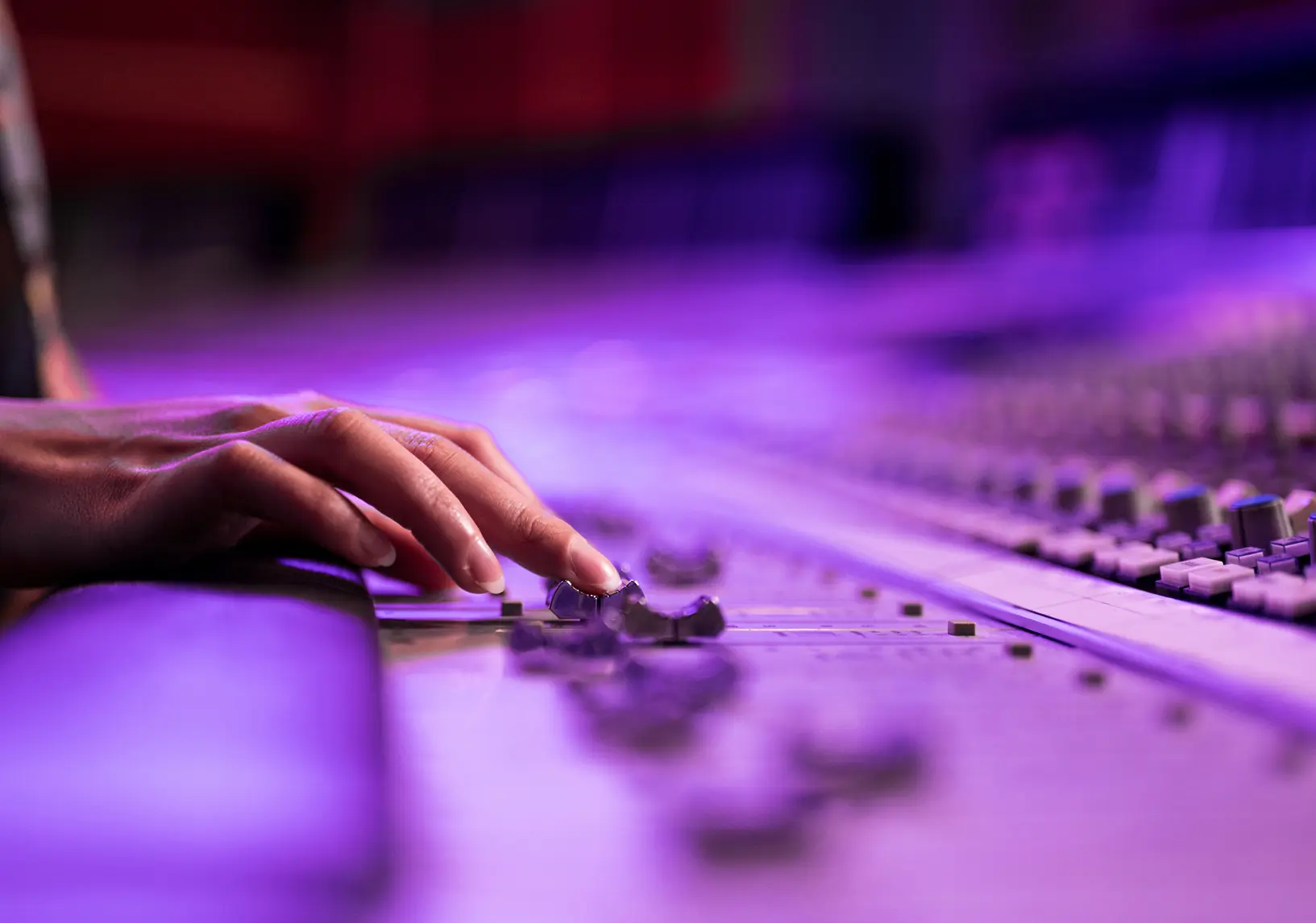 Hand adjusting audio mixing console sliders.